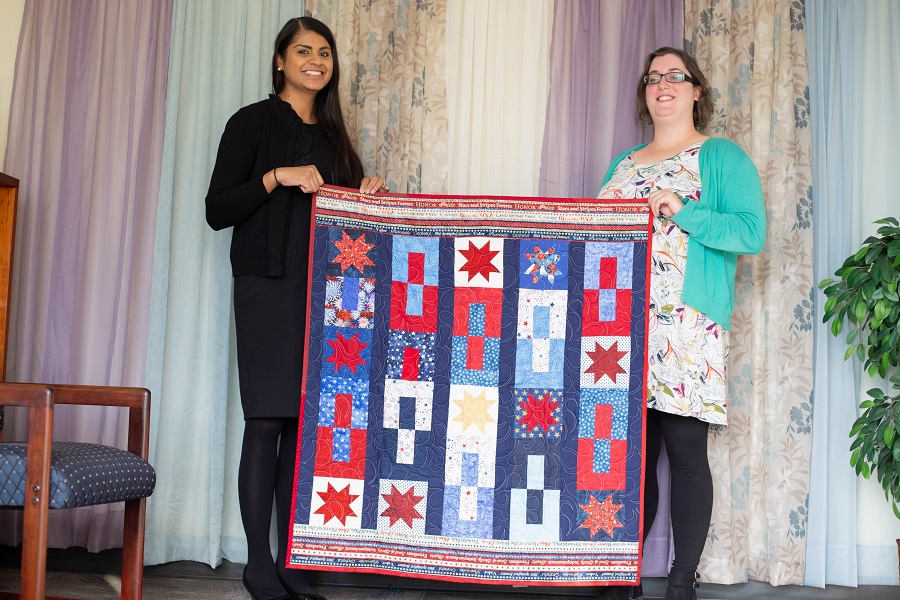 Ashima and Sarah hold a veteran's quilt